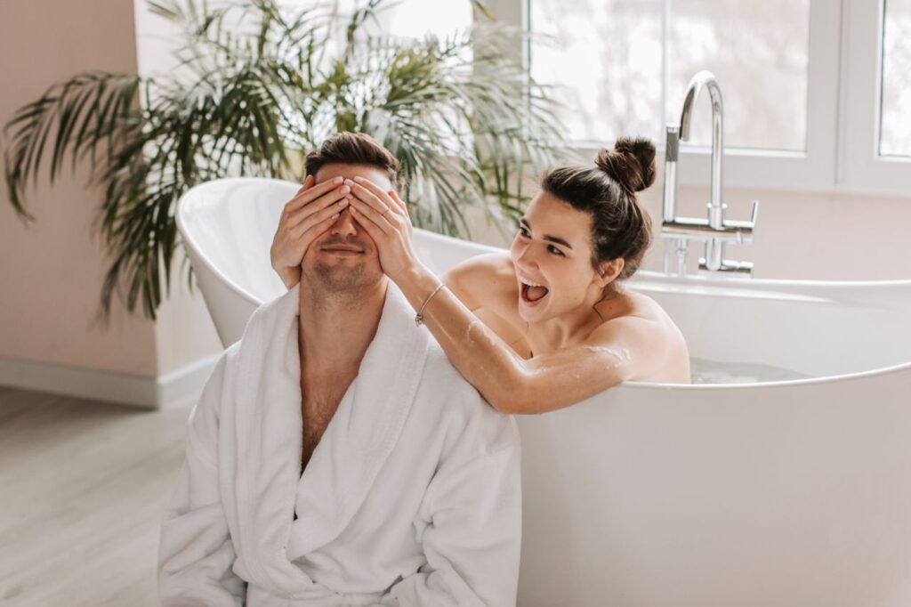 A cheerful couple having fun in the bathroom, with the woman covering the man's eyes playfully.